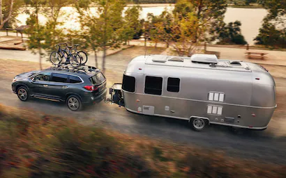 A Subaru Ascent towing a large travel trailer on a highway.